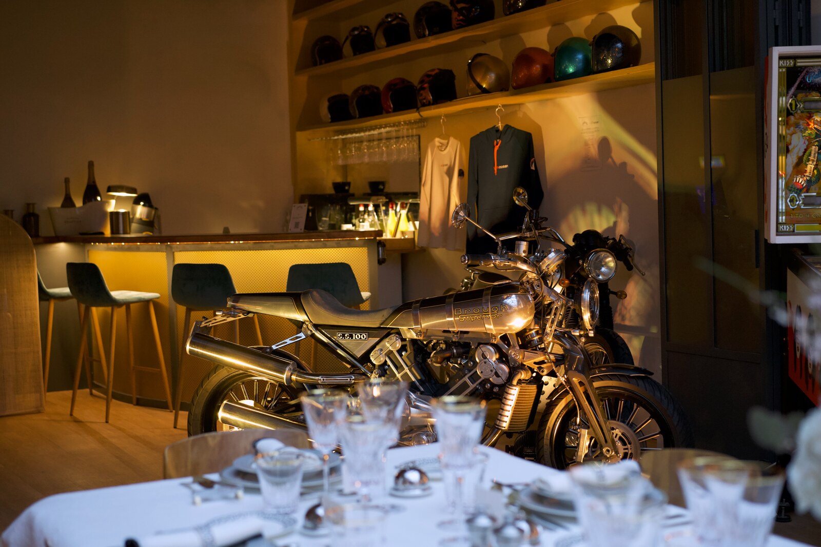 Le bar de La Fabrique Générale à la nuit tombée · moto Brough Superior, casques de collection, lumière tamisée