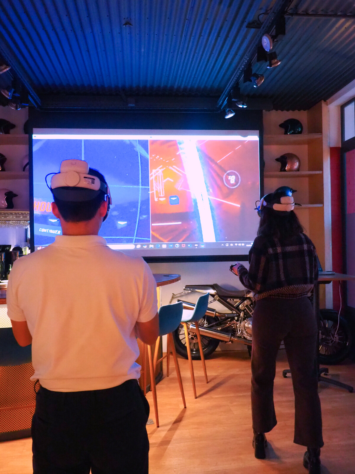 Animation réalité virtuelle à La Fabrique Générale, deux participants casque VR sur le dos face au grand écran, moto d'époque en décor